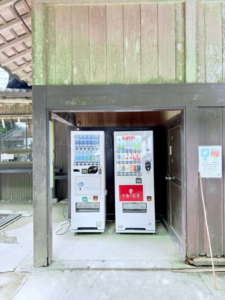 Two vending machines under a mossy wooden shelter at the summit of Mt. Atago