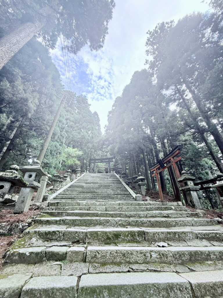 Stone staircase lined with lanterns and tall trees, leading up to the main shrine of Mt. Atago